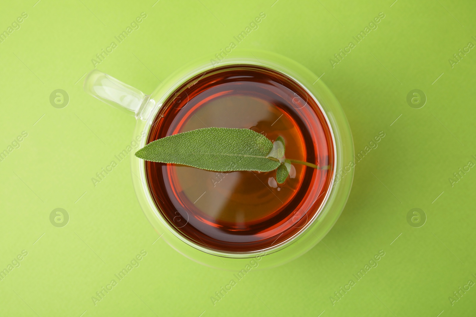 Photo of Aromatic herbal tea with sage in cup on green table, top view