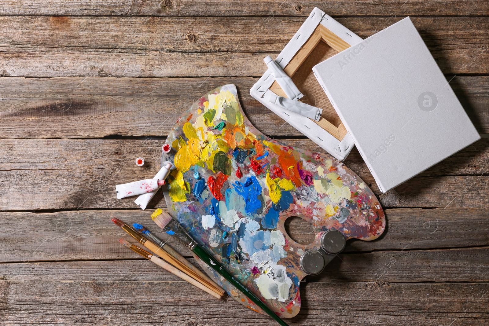 Photo of Artist's palette, brushes, paints and blank canvases on wooden table, flat lay