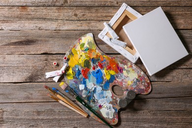 Artist's palette, brushes, paints and blank canvases on wooden table, flat lay