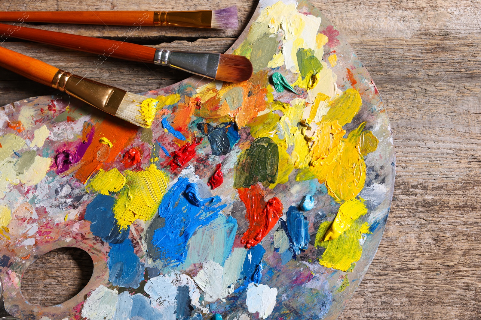 Photo of Artist's palette, brushes and paints on wooden table, flat lay