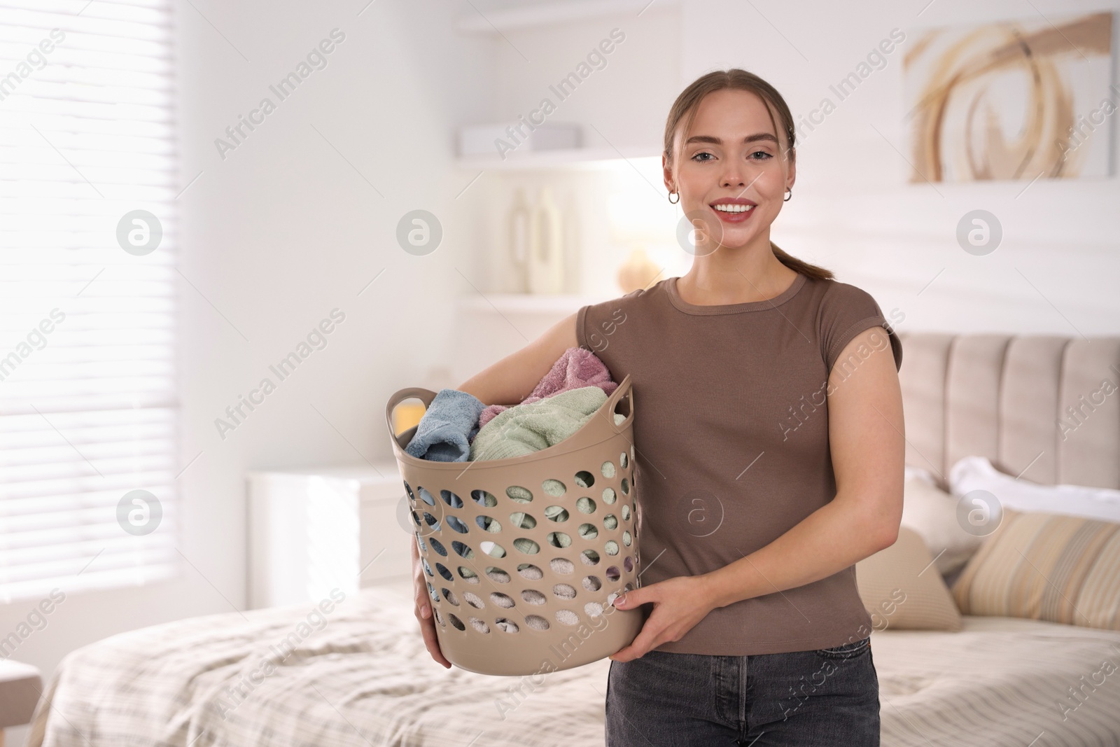 Photo of Happy young housewife with basket full of laundry at home