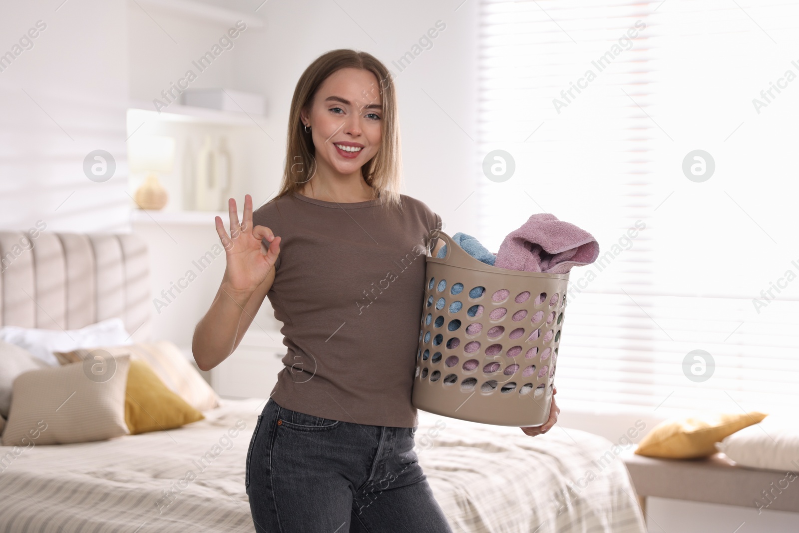 Photo of Happy young housewife with basket full of laundry at home