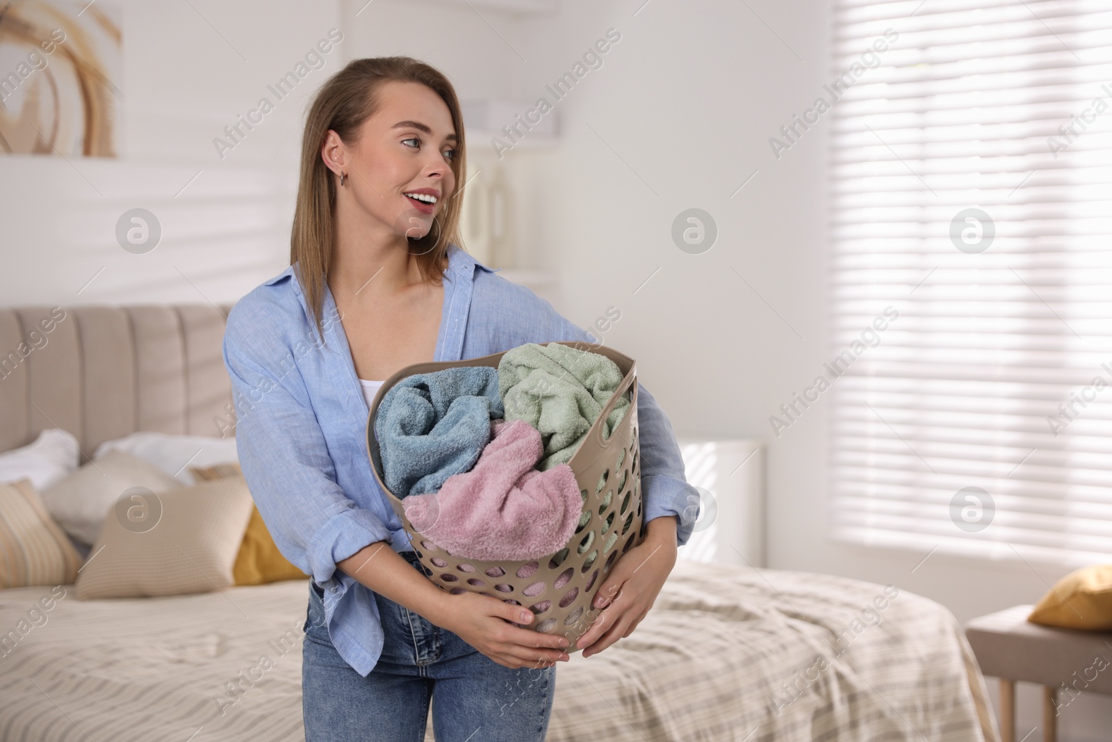 Photo of Happy young housewife with basket full of laundry at home