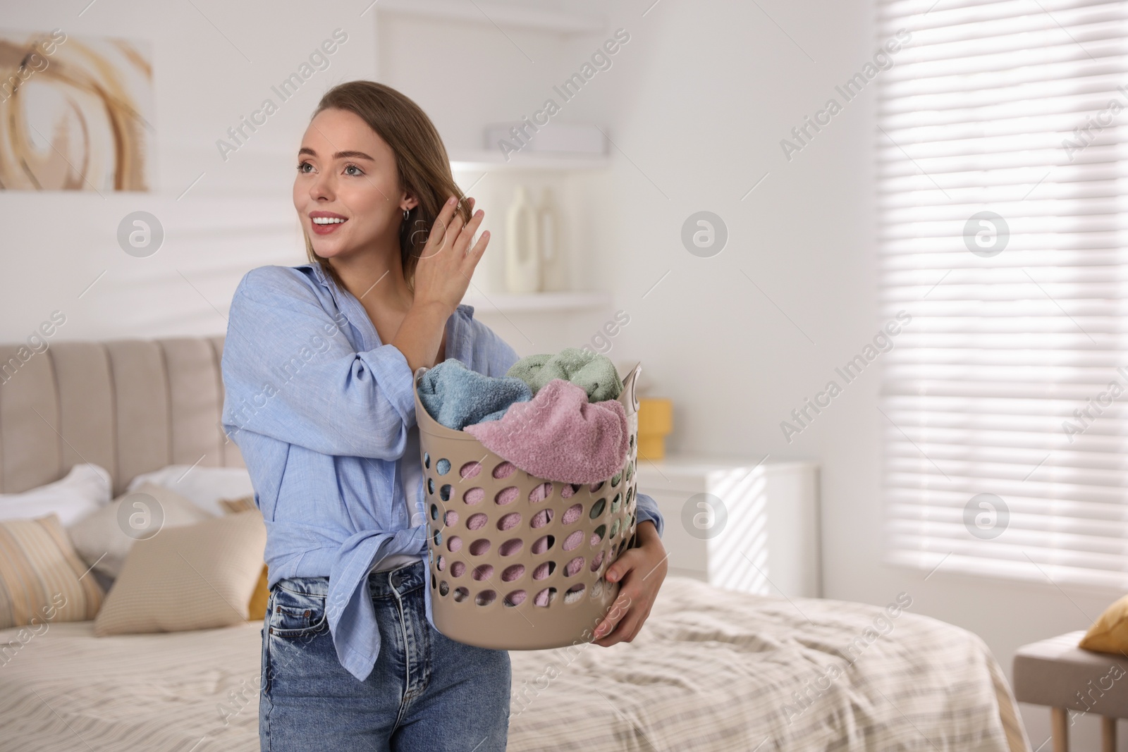 Photo of Happy young housewife with basket full of laundry at home