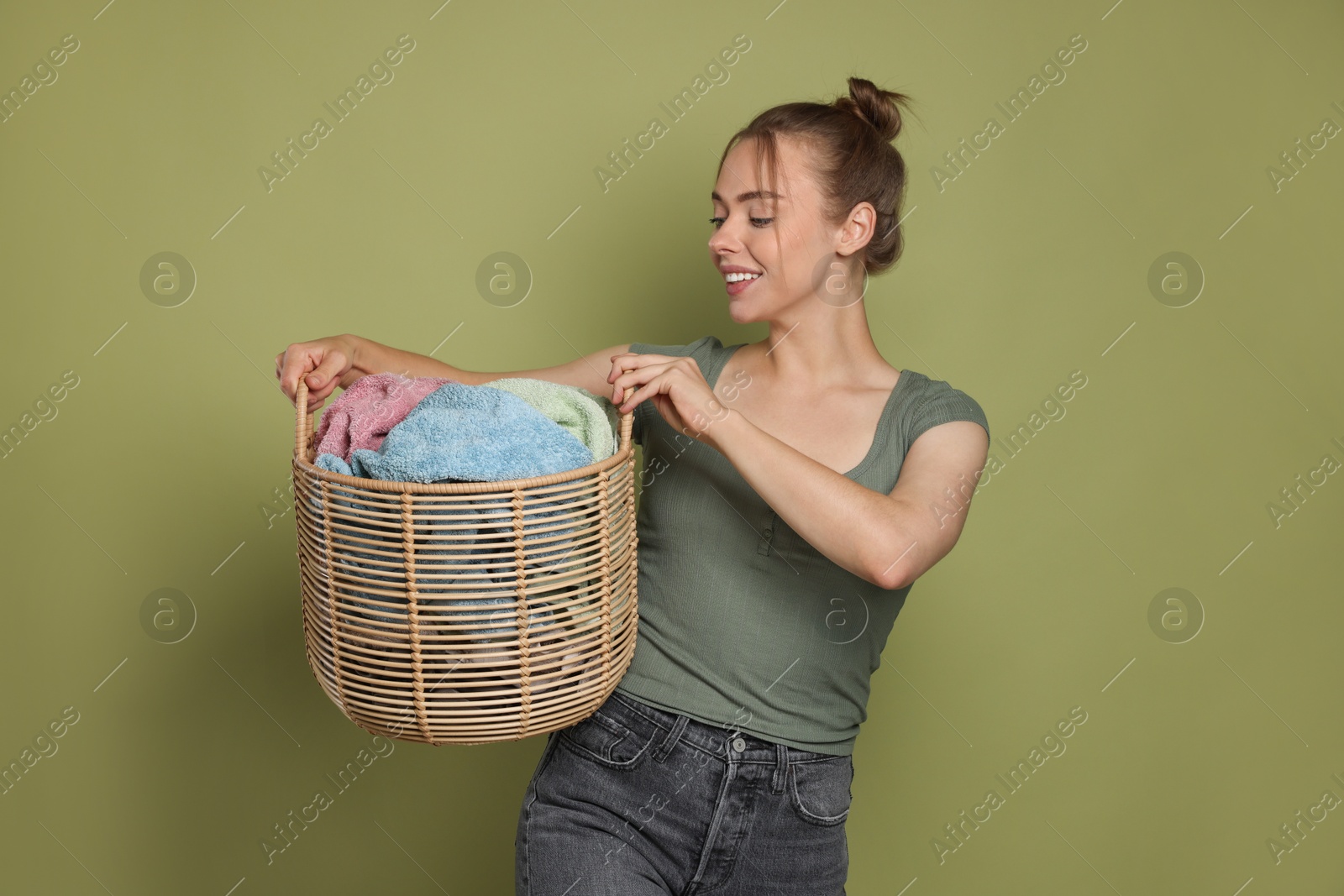 Photo of Happy young housewife with basket full of laundry on olive background