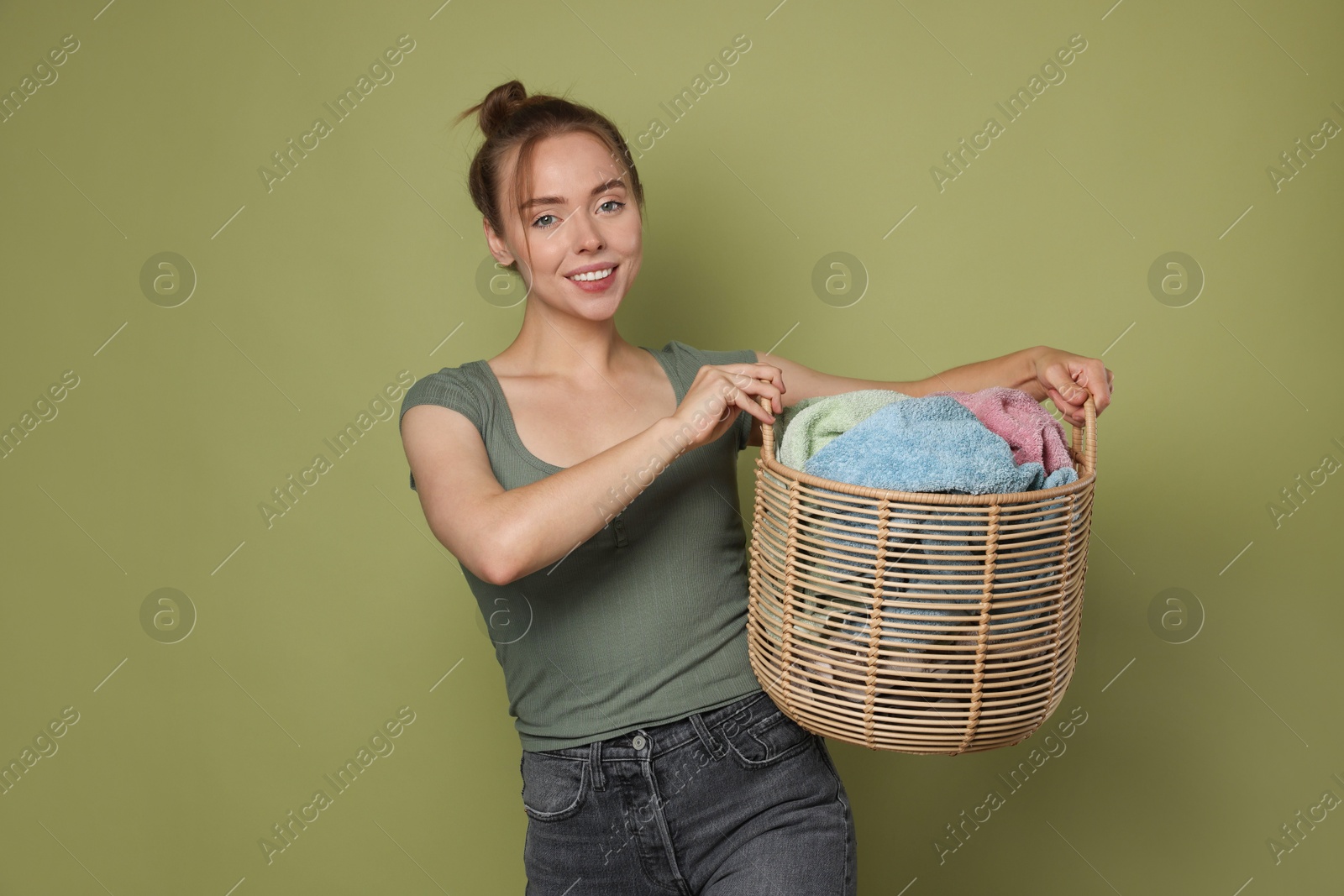 Photo of Happy young housewife with basket full of laundry on olive background