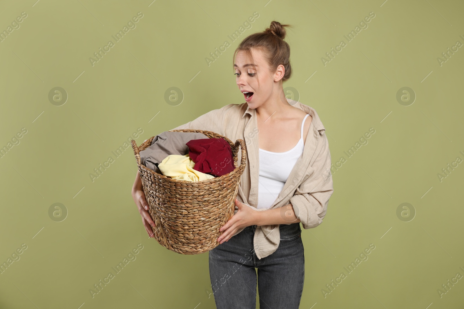 Photo of Emotional housewife with basket full of laundry on olive background