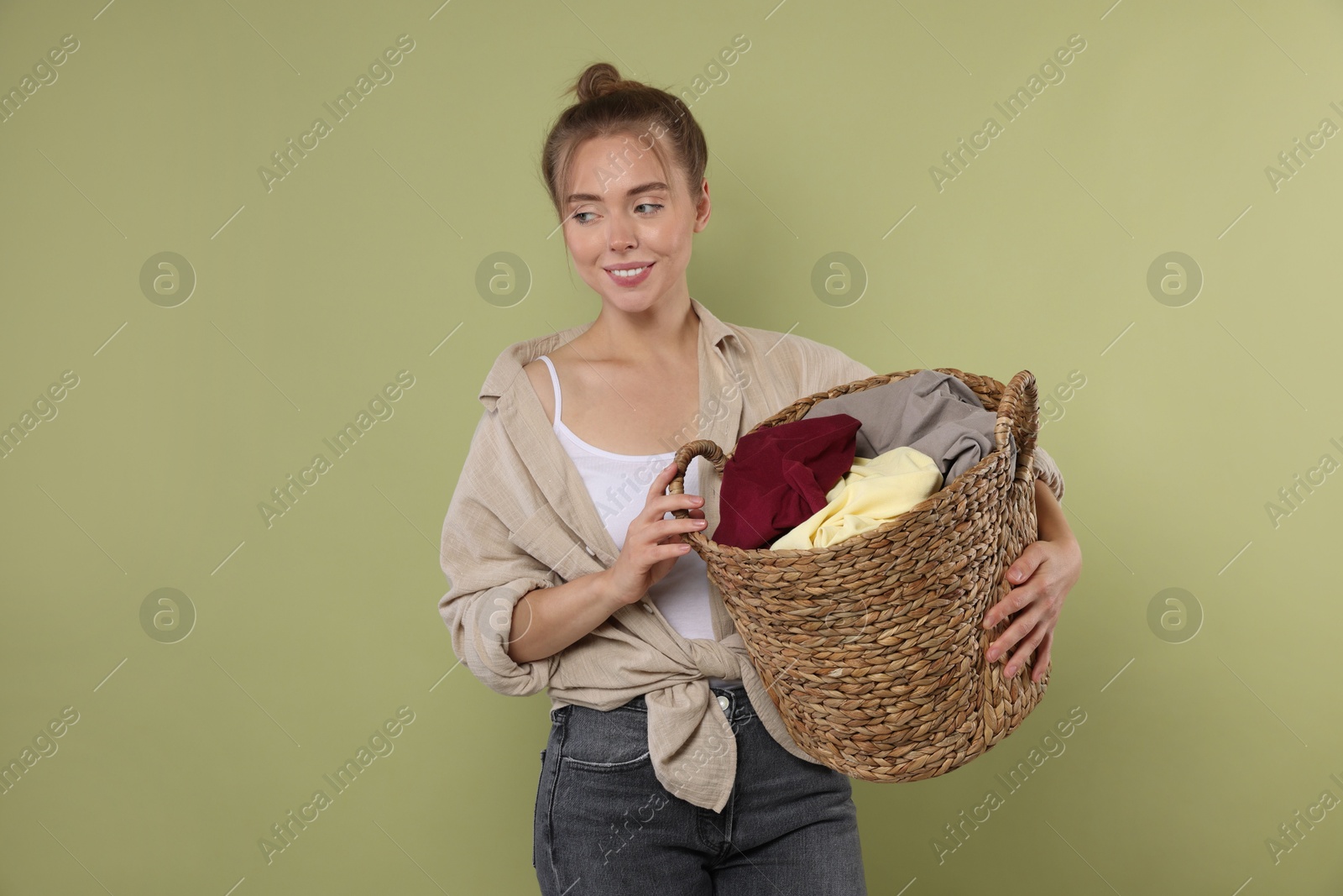 Photo of Happy young housewife with basket full of laundry on olive background