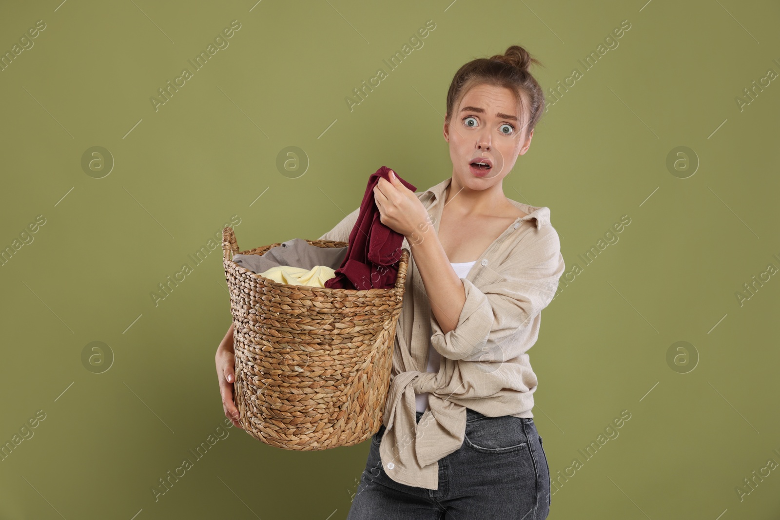 Photo of Emotional housewife with basket full of laundry on olive background