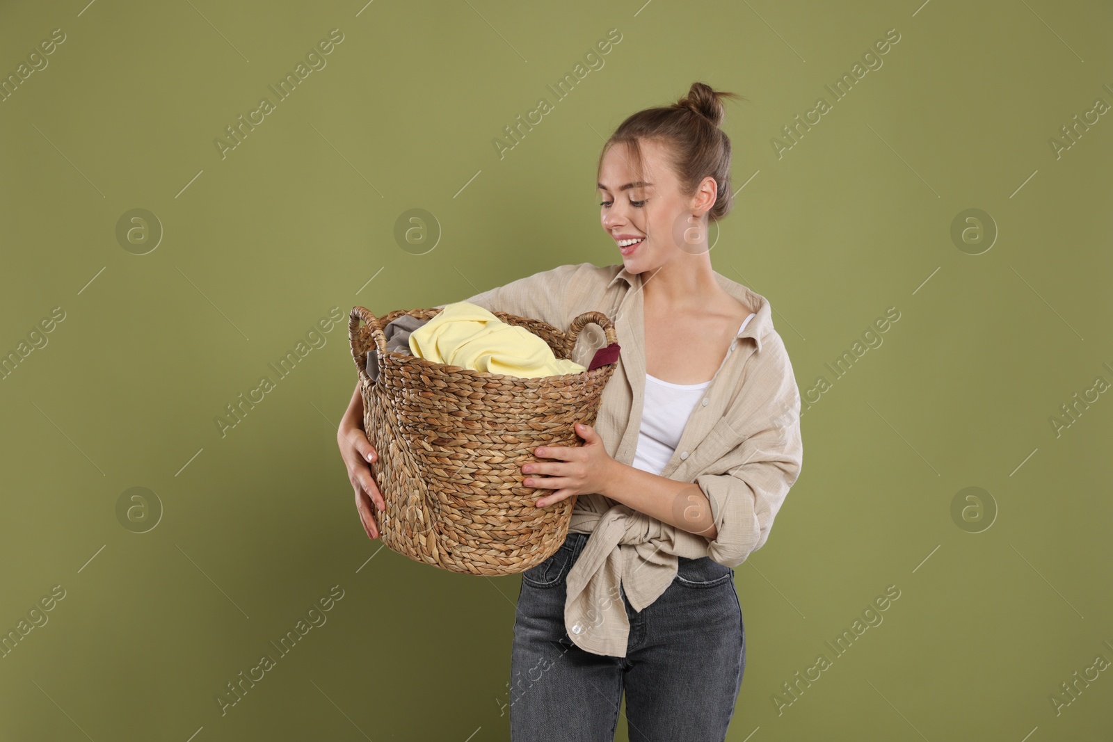 Photo of Happy young housewife with basket full of laundry on olive background