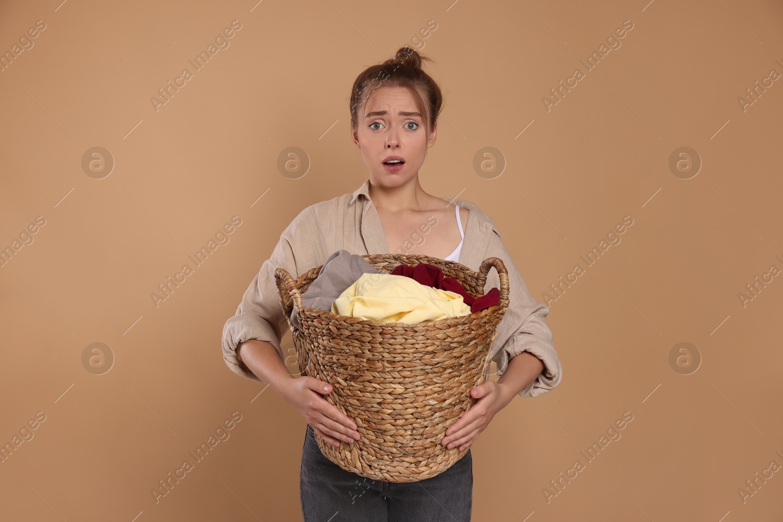 Photo of Tired housewife with basket full of laundry on pale orange background