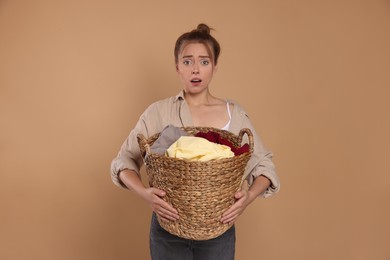 Tired housewife with basket full of laundry on pale orange background