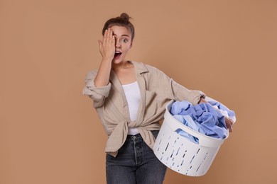 Emotional housewife with basket full of laundry on pale orange background