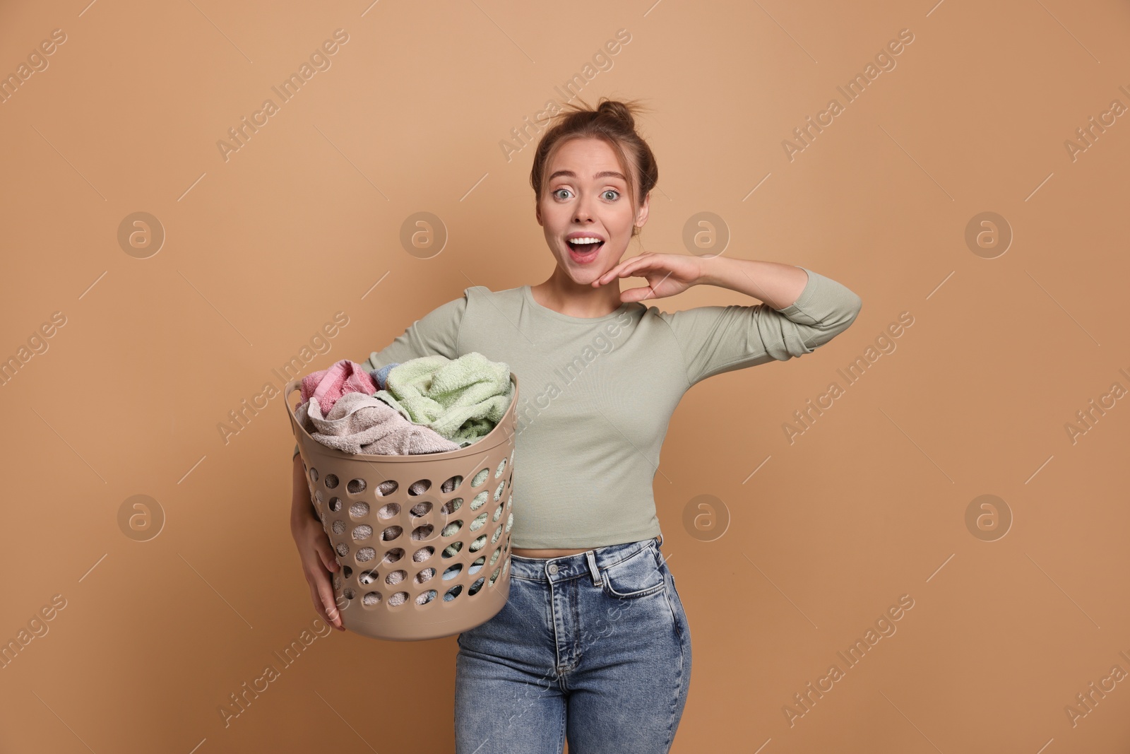 Photo of Happy young housewife with basket full of laundry on pale orange background