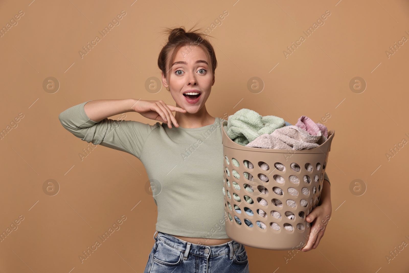 Photo of Happy young housewife with basket full of laundry on pale orange background