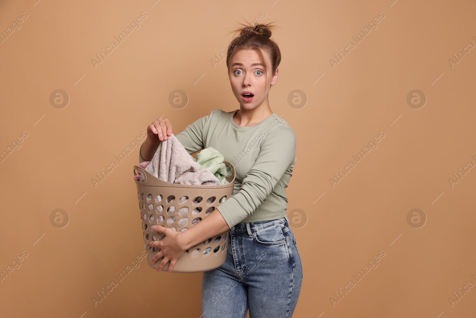 Photo of Emotional housewife with basket full of laundry on pale orange background