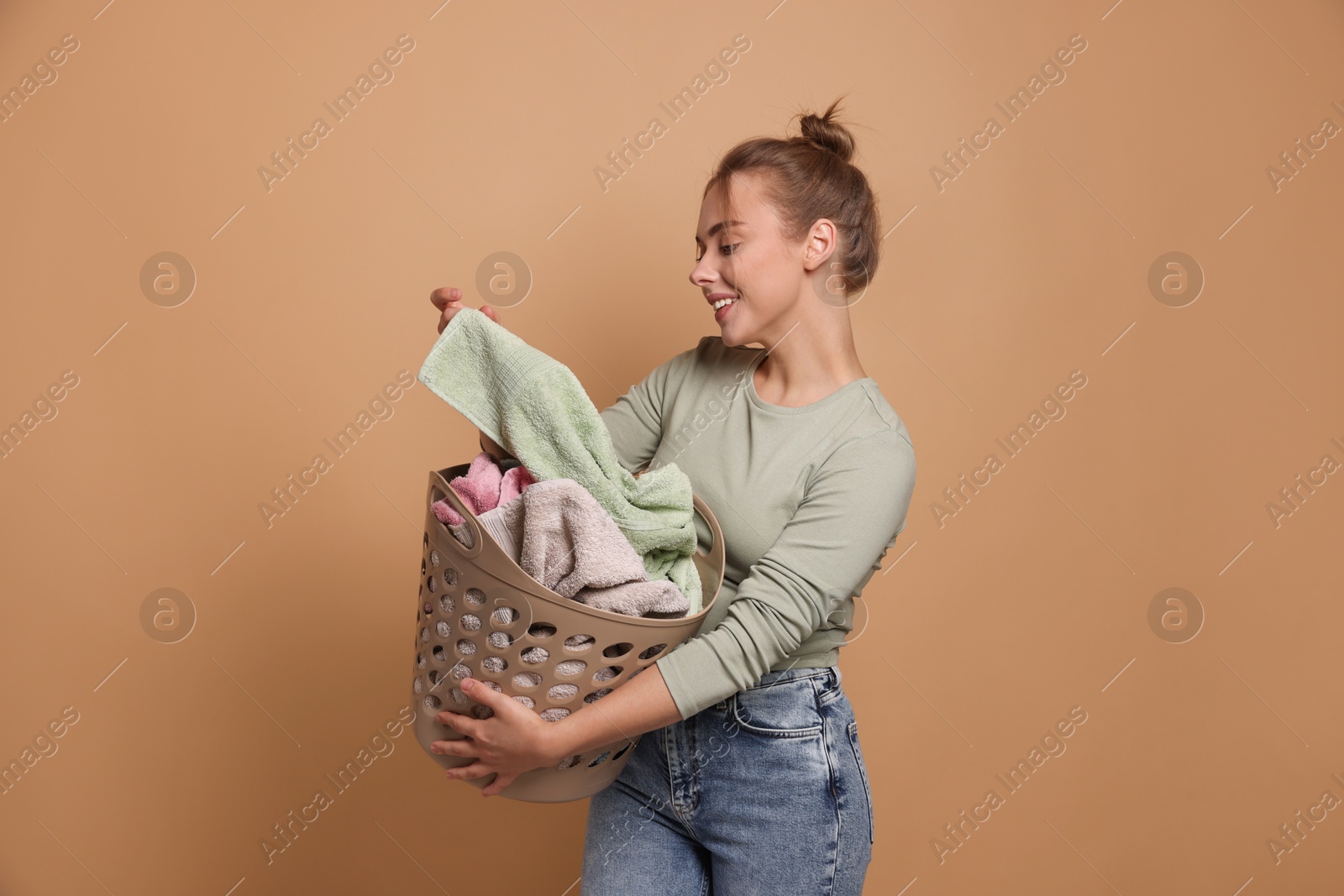 Photo of Happy young housewife with basket full of laundry on pale orange background