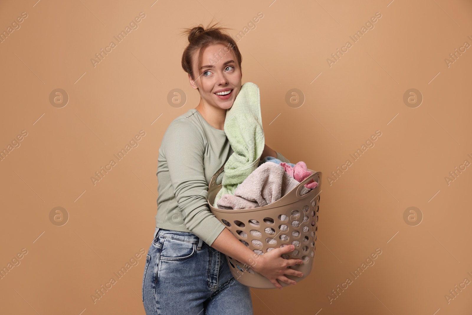 Photo of Happy young housewife with basket full of laundry on pale orange background