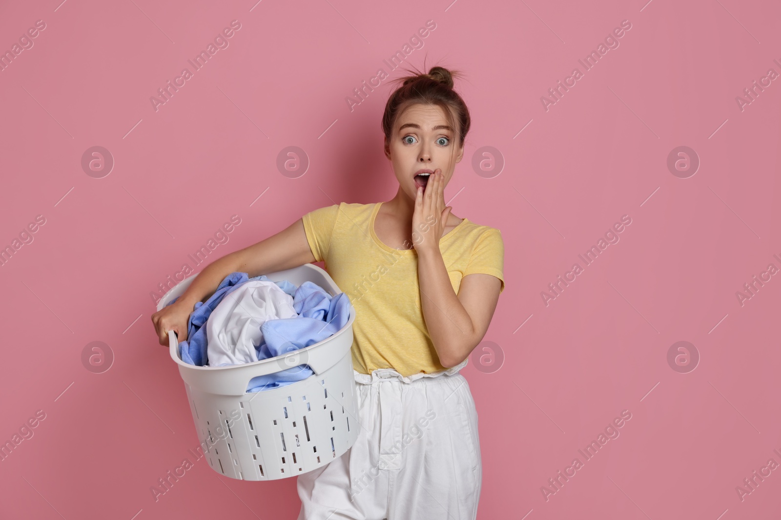 Photo of Emotional housewife with basket full of laundry on pale pink background