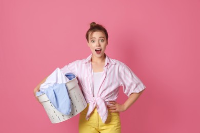 Emotional housewife with basket full of laundry on pale pink background