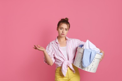 Tired housewife with basket full of laundry on pale pink background