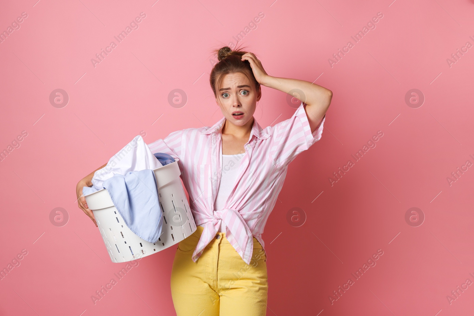 Photo of Tired housewife with basket full of laundry on pale pink background