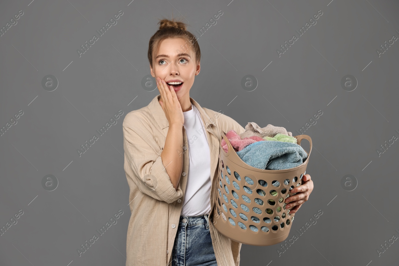 Photo of Happy young housewife with basket full of laundry on grey background