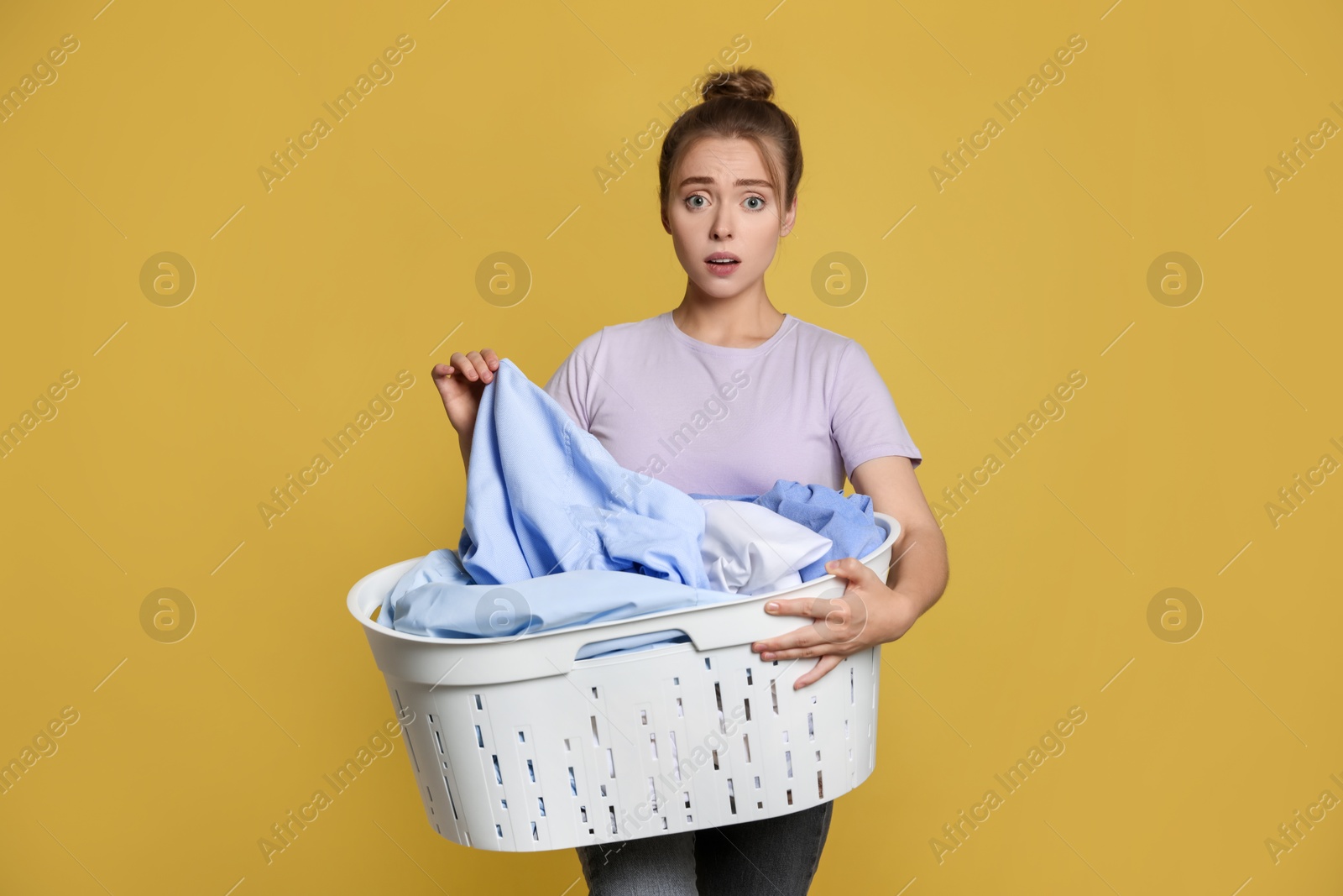 Photo of Tired housewife with basket full of laundry on yellow background