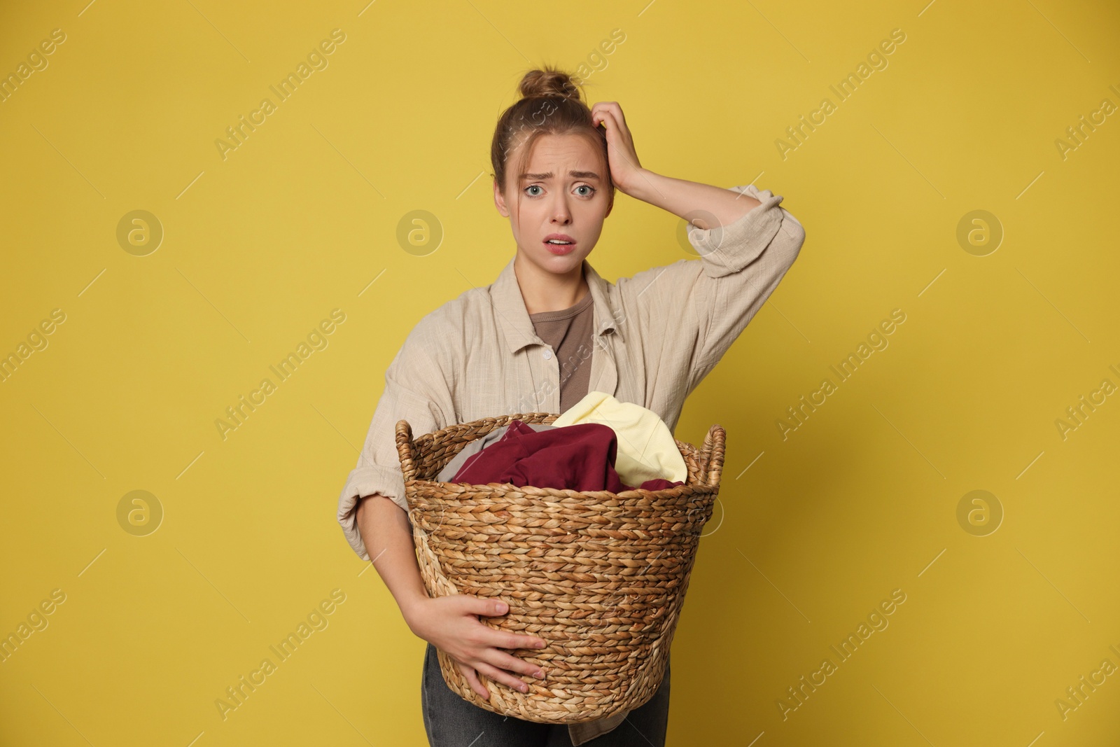 Photo of Tired housewife with basket full of laundry on yellow background