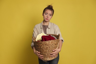 Photo of Tired housewife with basket full of laundry on yellow background