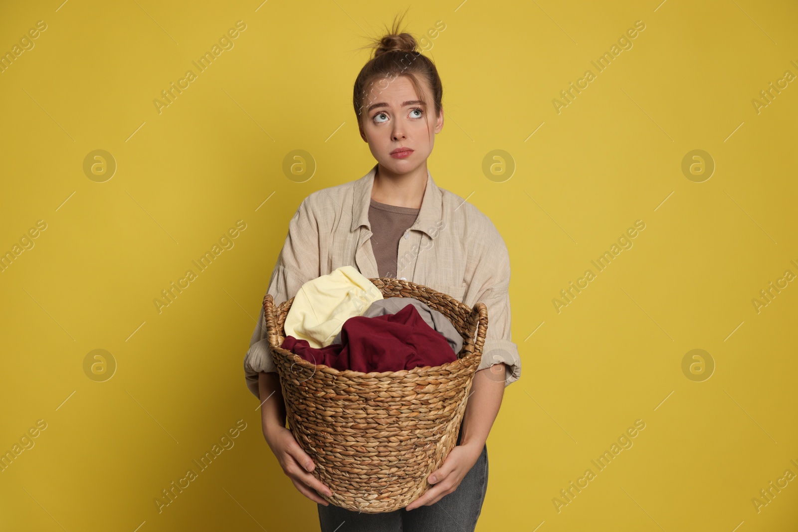 Photo of Tired housewife with basket full of laundry on yellow background