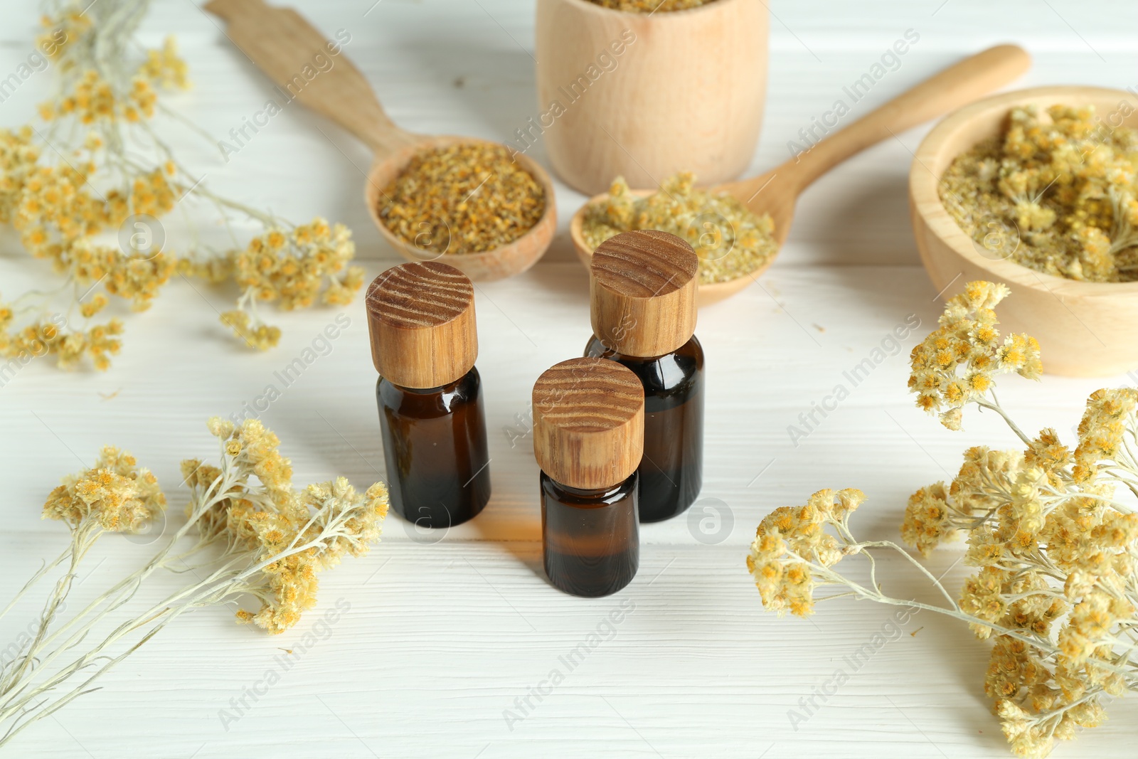 Photo of Tinctures in bottles and helichrysum flowers on white wooden table