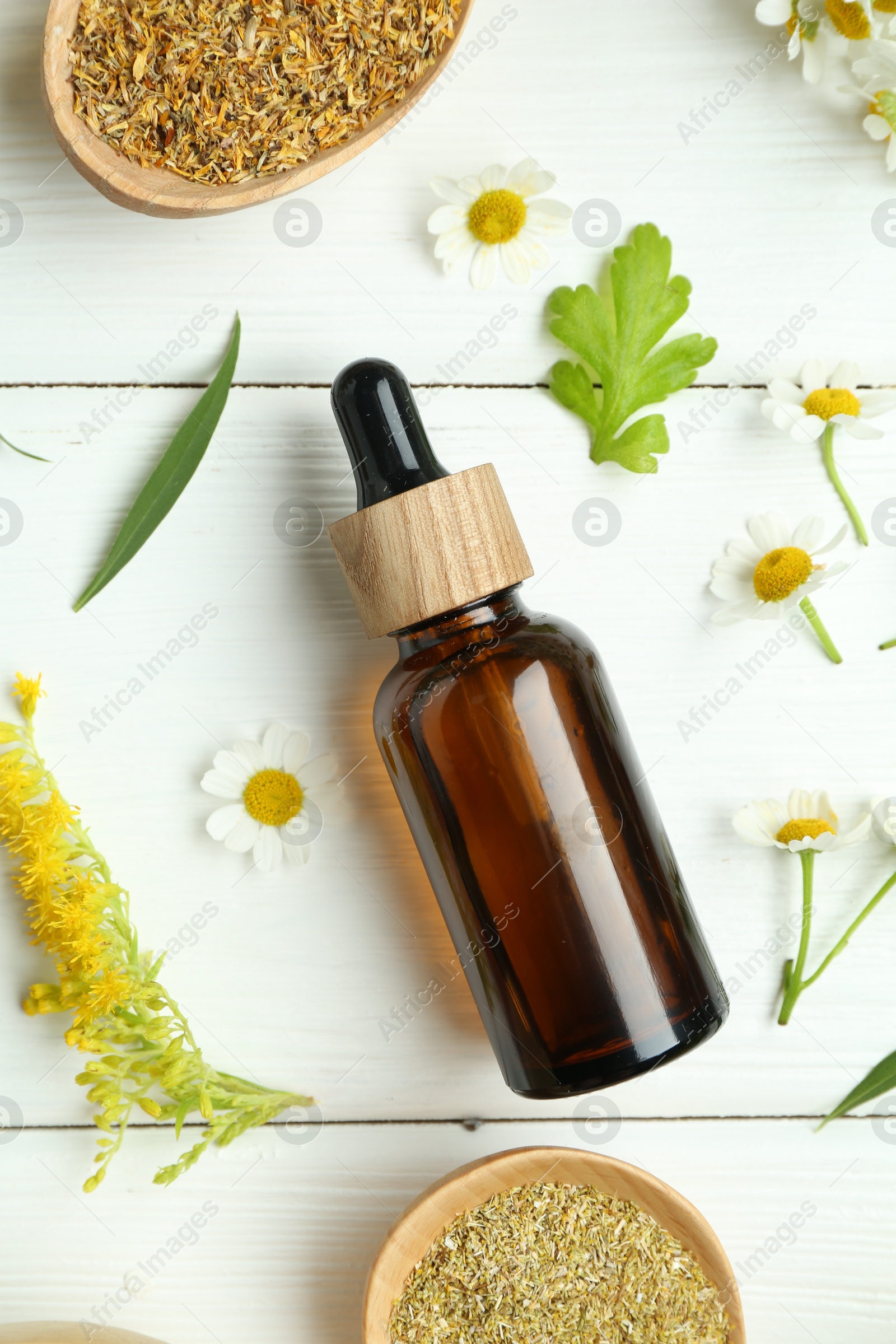 Photo of Tincture in bottle, goldenrod flower and chamomiles on white wooden table, flat lay