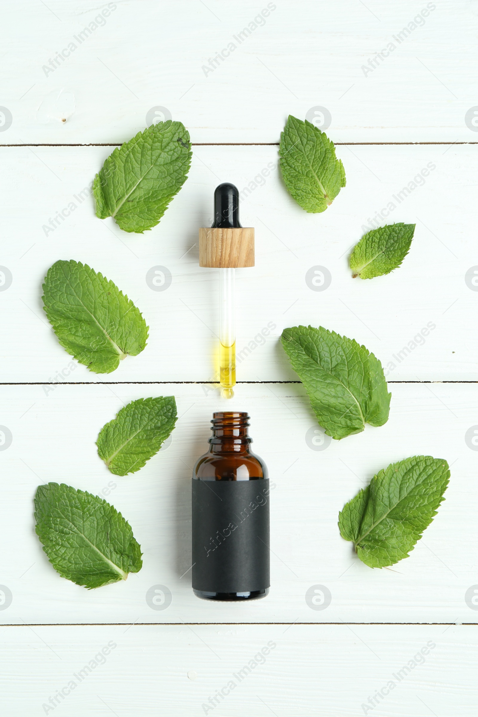 Photo of Dripping tincture from pipette into bottle and mint on white wooden table, flat lay