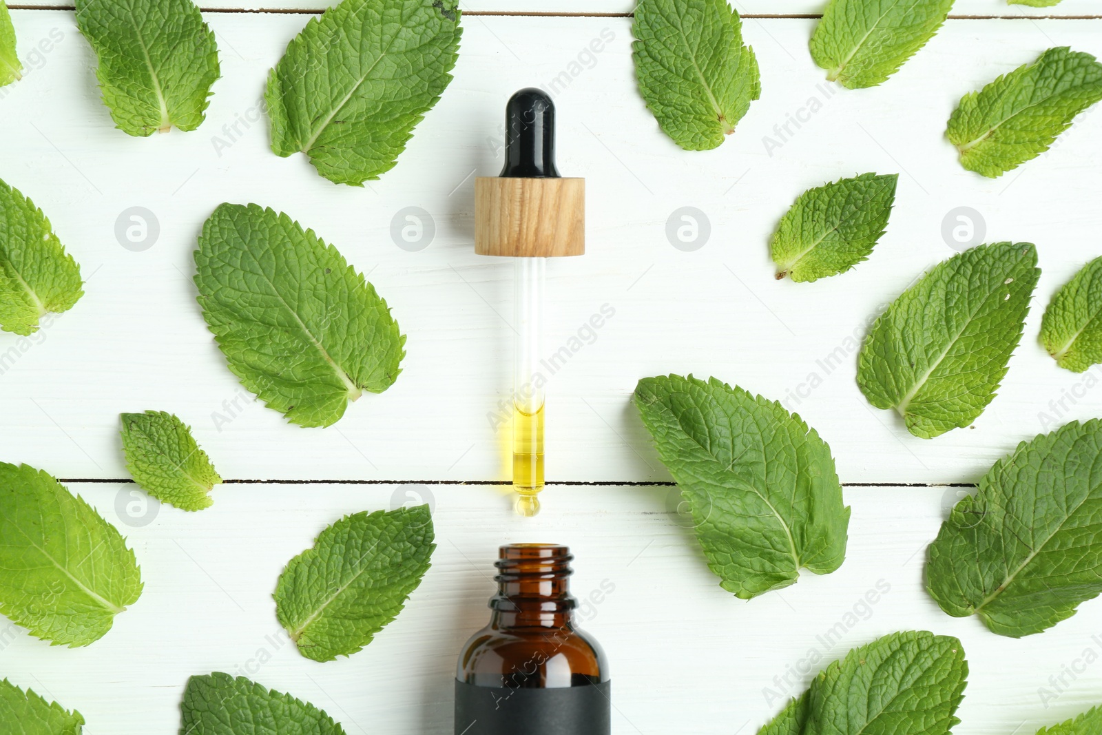 Photo of Dripping tincture from pipette into bottle and mint on white wooden table, flat lay