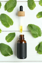 Photo of Dripping tincture from pipette into bottle and mint on white wooden table, flat lay