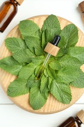 Photo of Tinctures in bottles, pipette and mint on white wooden table, top view