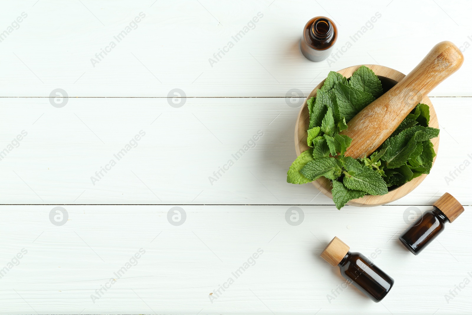 Photo of Tinctures in bottles, mortar, pestle and mint on white wooden table, flat lay. Space for text