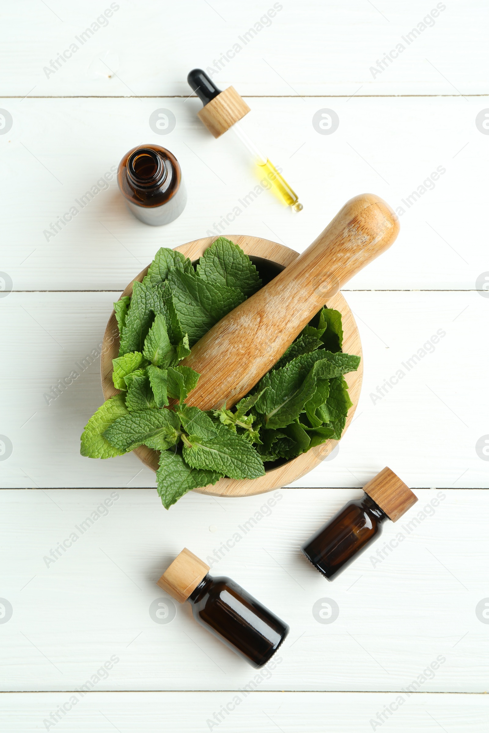 Photo of Tinctures in bottles, pipette, mortar, pestle and mint on white wooden table, flat lay