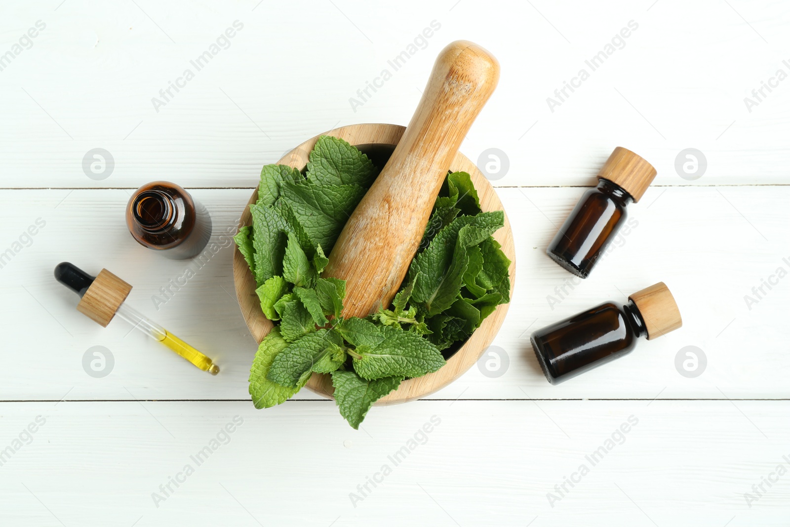 Photo of Tinctures in bottles, pipette, mortar, pestle and mint on white wooden table, flat lay