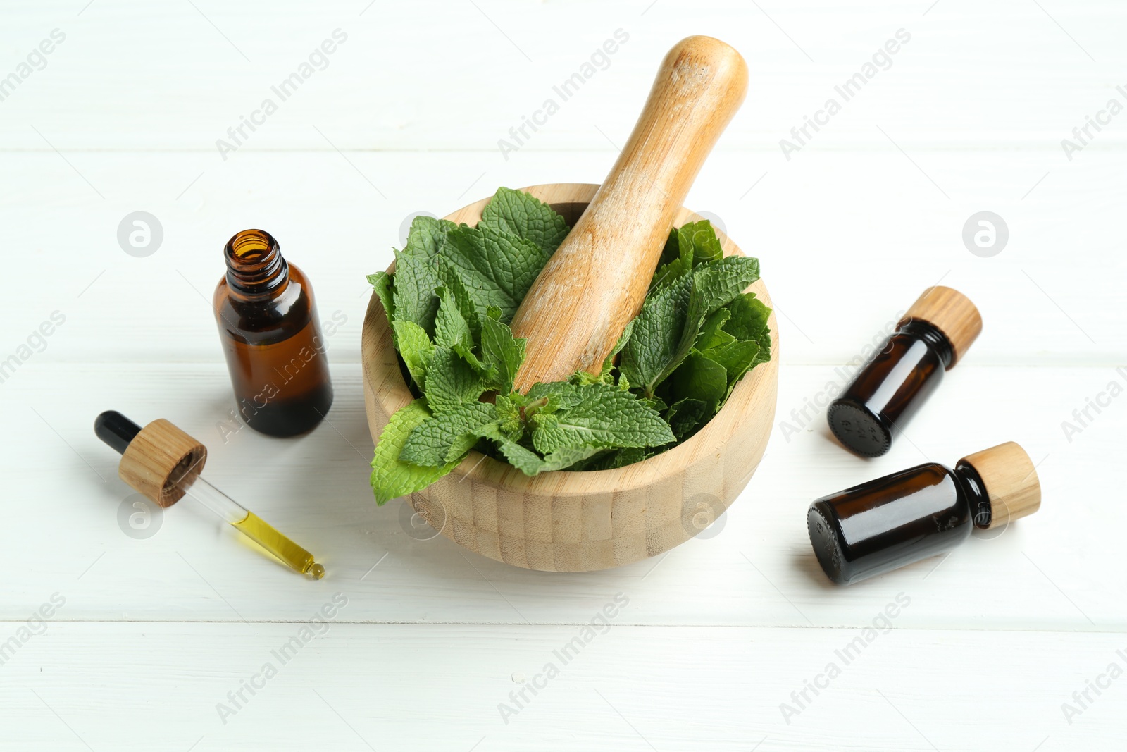 Photo of Tinctures in bottles, pipette, mortar, pestle and mint on white wooden table