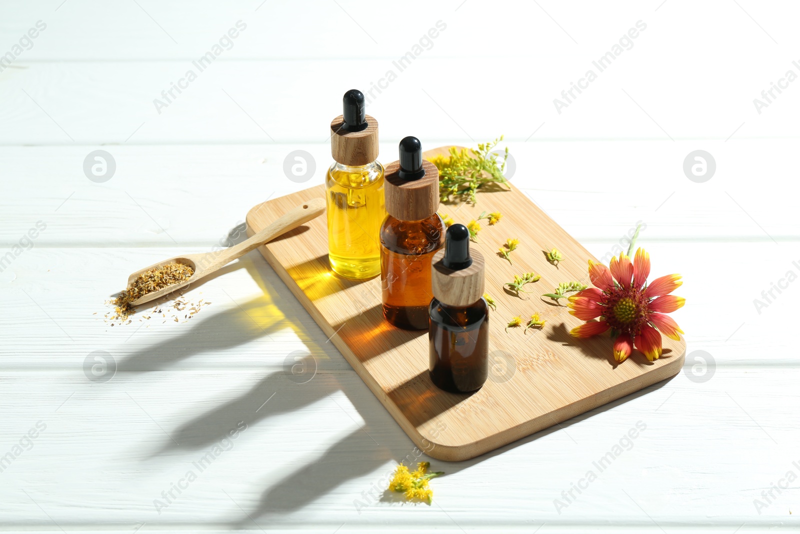 Photo of Tinctures in bottles, goldenrods and gaillardia flower on white wooden table