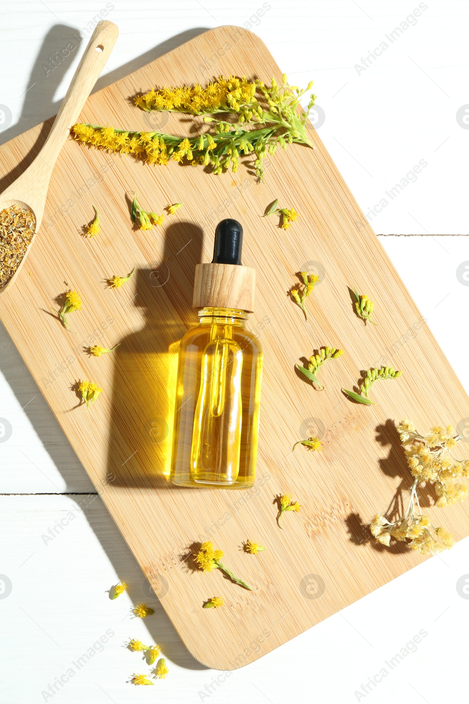 Photo of Tincture in bottle, goldenrods and helichrysum flowers on white wooden table, top view