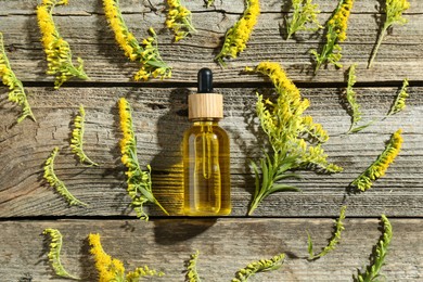 Photo of Tincture in bottle and goldenrod flowers on wooden table, flat lay