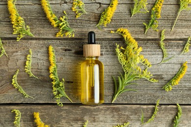 Photo of Tincture in bottle and goldenrod flowers on wooden table, flat lay