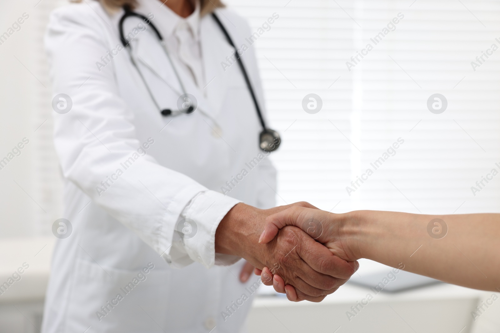 Photo of Senior doctor shaking hands with patient in hospital, closeup