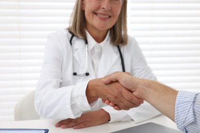 Photo of Senior doctor shaking hands with patient in hospital, closeup