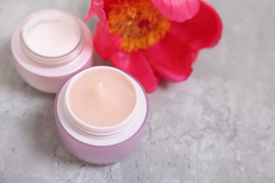 Photo of Jars of creams and peony flower on gray table. Space for text