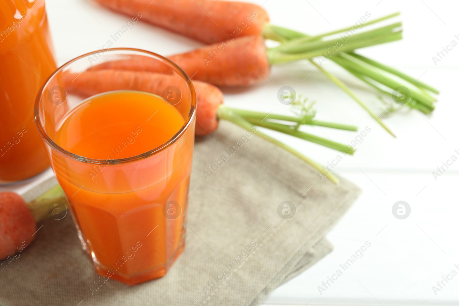 Photo of Healthy juice and fresh carrot on white wooden table. Space for text