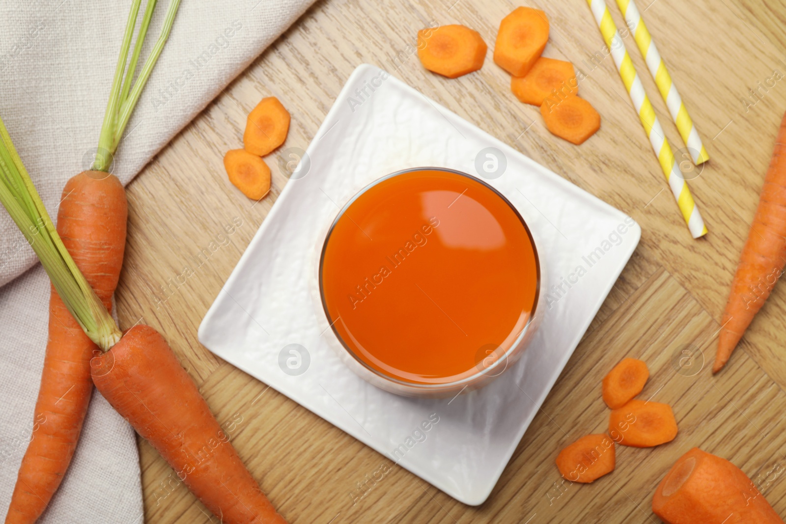 Photo of Healthy juice in glass and fresh carrot on wooden table, flat lay